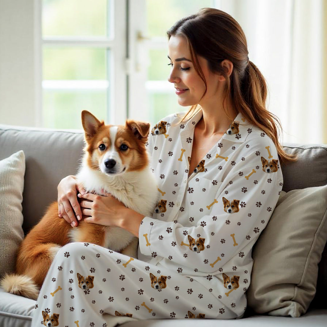 Donna che indossa un set pigiama bianco personalizzato con il muso del suo cane, impronte e ossi, mentre tiene in braccio un cane marrone e bianco sul divano